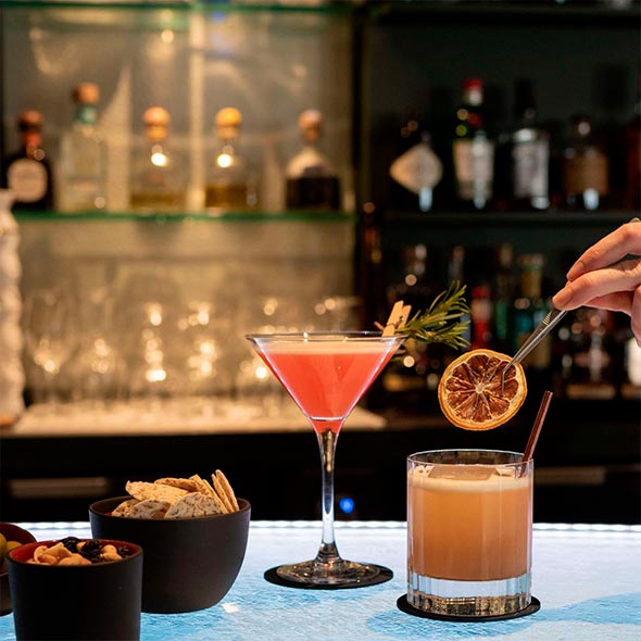 Classic interior of Bar Annapurna: a circular wooden bar counter with red leather stools, a massive carved stone fireplace, a green velvet armchair, and a soft red sofa.