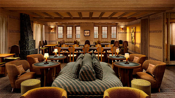 Luxurious alpine-style lounge restaurant with wood paneling, a large central sofa, armchairs, small tables with lamps, and a dining area by a row of windows