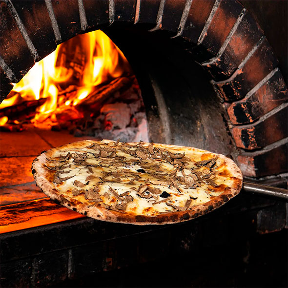 Thin crust pizza with truffles and cheese being taken out of a hot wood-fired oven.