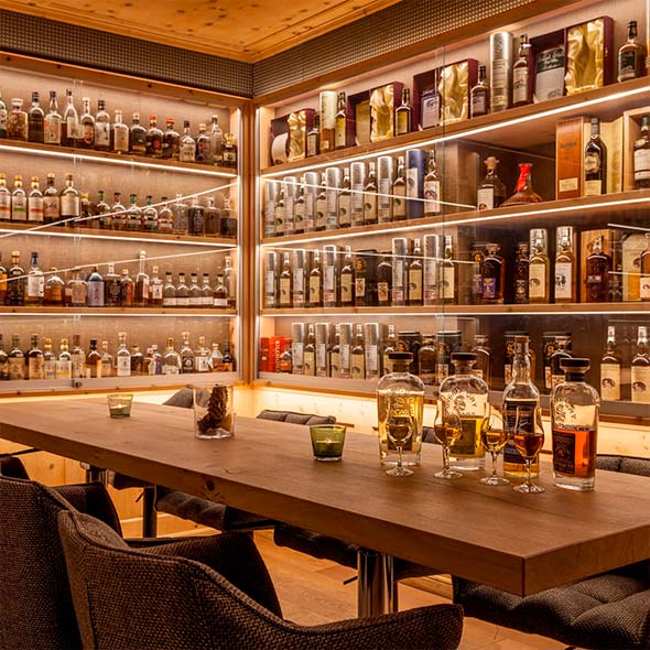 Interior of Devil&rsquo;s Place bar featuring a wooden tasting table and floor-to-ceiling illuminated glass shelves filled with an immense collection of whisky bottles.