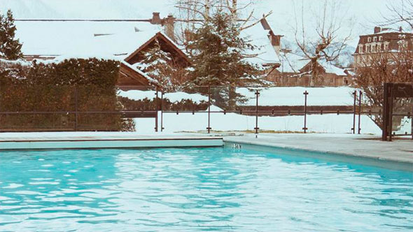 Heated outdoor swimming pool at Hameau Albert 1er hotel in Chamonix, surrounded by snow-covered trees and traditional chalets
