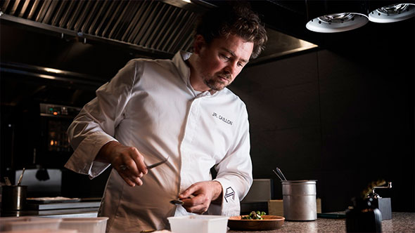 Close-up of Chef Jean-Remi Caillon, wearing a white chef&rsquo;s jacket, intensely focused on finishing a gourmet dish in the La Table de l&rsquo;Annapurna kitchen, highlighting the fine dining experience.