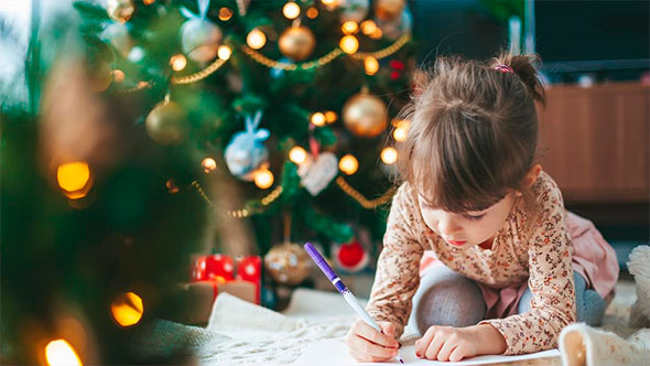 Close-up of a young girl writing a letter to Santa, sitting on the floor against a backdrop of a festive Christmas tree in the hotel&rsquo;s kids&rsquo; club.