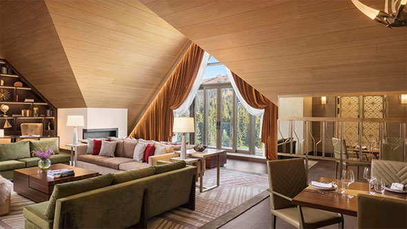 Luxurious living room of a duplex suite (penthouse) at Viceroy Kopaonik in alpine style with wooden ceiling cladding, a fireplace, and forest views.