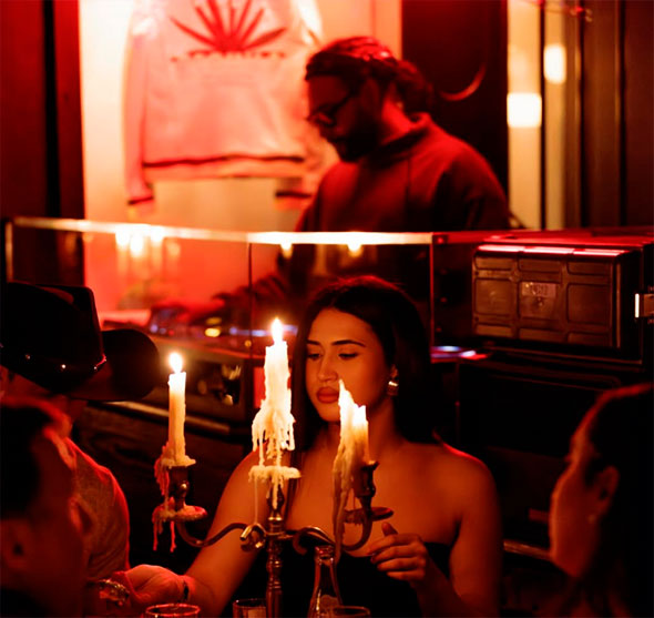 Atmospheric photo of La Mangeoire’s interior during a party: a girl sits at a table lit by melting candles in a candelabra, with a DJ working the booth in the background.