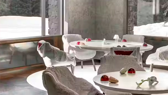 Minimalist dining area: white round tables and soft-upholstered chairs, large windows overlooking a snowy landscape, and stylish red decorative elements