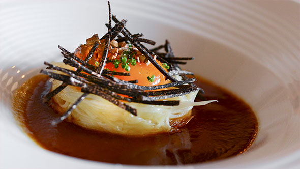 Exquisite dish: a small mound of finely chopped herbs, greens, and meat/mushrooms, topped with a green pepper pod (or cucumber), served on a round wooden plate