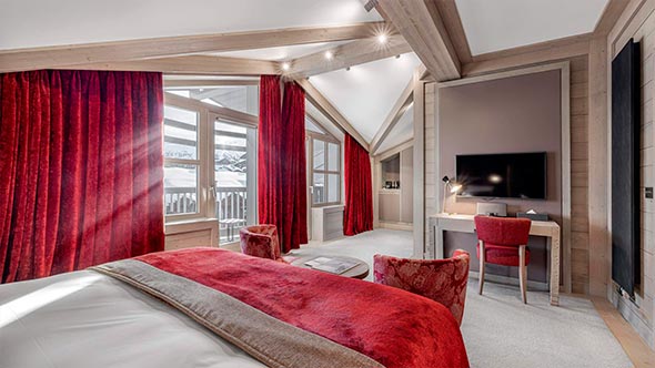 Luxurious interior of a suite at Le K2 Djola hotel featuring panoramic windows, wood finishes, and vibrant red accents. / Роскошный интерьер номера в отеле Le K2 Djola с панорамными окнами, отделкой из дерева и яркими красными акцентами.