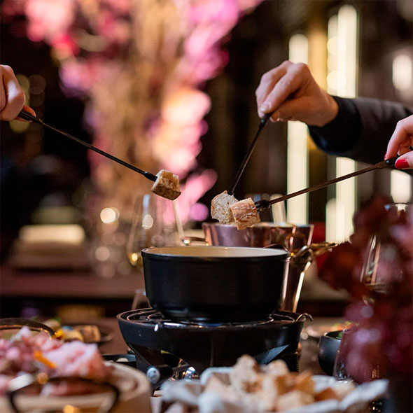 Guests enjoying a cheese fondue dinner at Le Bottleneck restaurant, using long forks to dip bread pieces into the communal pot.