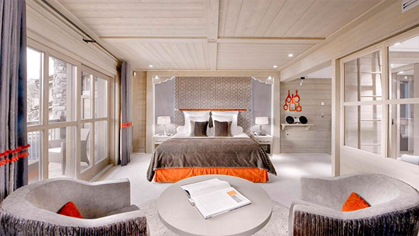 Luxurious suite bedroom at Le K2 featuring a King-size bed, wood paneling, elegant furniture, and access to a terrace with mountain views.