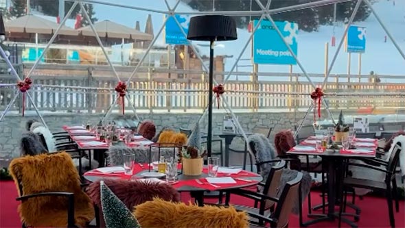 Cozy dining interior (likely a geodesic dome or tent) of Le Tremplin bar: tables covered with red tablecloths, chairs decorated and draped with fluffy fur blankets (khaki, white, brown).