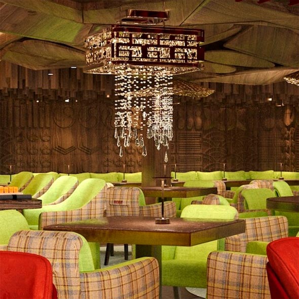 Elegant interior of the bar/lounge at the Maya Hotel Courchevel 1850 featuring soft green armchairs, checkered upholstery, wood paneling, and a large crystal chandelier.