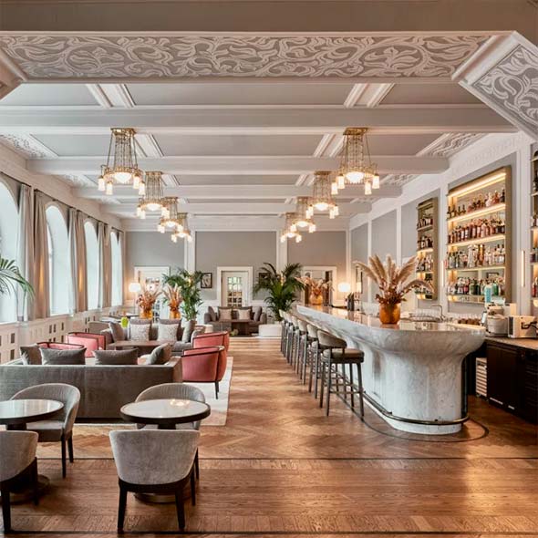 Stylish and bright interior of N/5 The Bar featuring a high ceiling, decorative stucco, a long white marble bar counter, and a lounge area with soft seating.