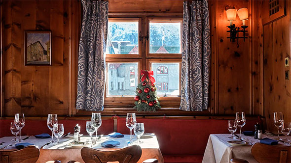Cozy lounge area of Patrizier Stuben restaurant featuring a leather sofa, wood paneling, a roaring fireplace, and a low table set with snacks and drinks.