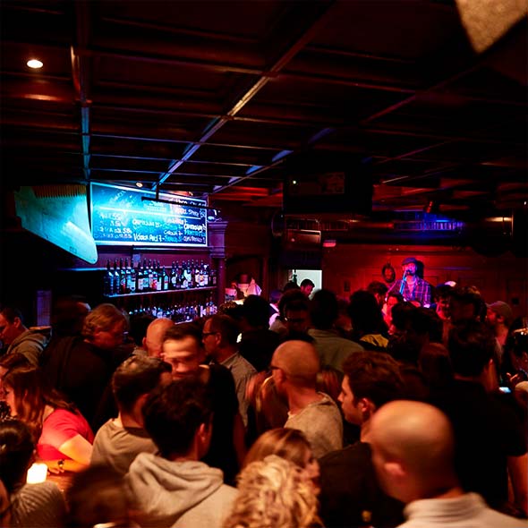 Crowded St&uuml;bli Bar interior with dim red lighting, featuring a bar counter against the far wall and live music being played.