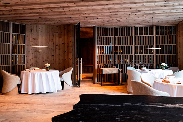 Modern restaurant interior with wooden panels and semicircular partitions, white tablecloths, and plush chairs.