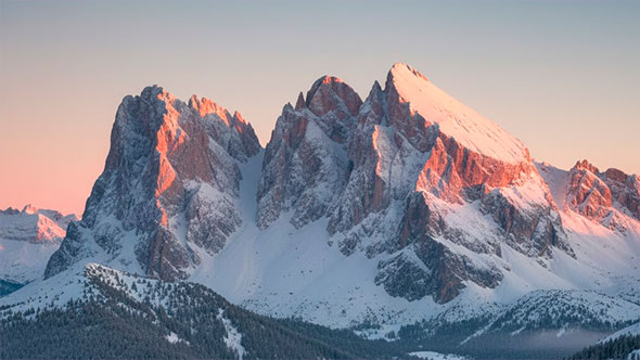 Snow-capped, jagged Dolomite peaks at sunrise, illuminated with soft pink and peach colours, illustrating the L’Enrosadira phenomenon.