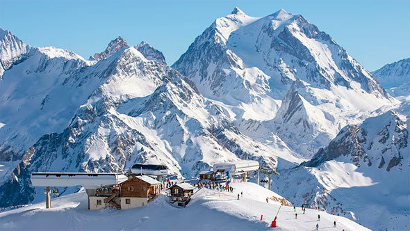 Majestic panoramic view of the snow-covered Alps and the high-altitude resort of Val Thorens, showing the ski station, lifts, and skiers on the slope on a sunny winter day.