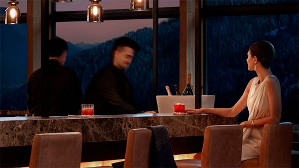 A woman enjoying a cocktail at a luxury Dolomites hotel bar (Lefay Resort) with staff, overlooking the snowy mountain view at night.