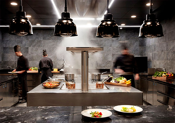 Modern professional show kitchen at Lefay Resort, with chefs preparing food and two plated gourmet dishes in the foreground.