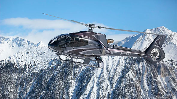 Luxury private charter helicopter flying over the snowy peaks of the Dolomites under a clear blue sky (Heli-ski tour).