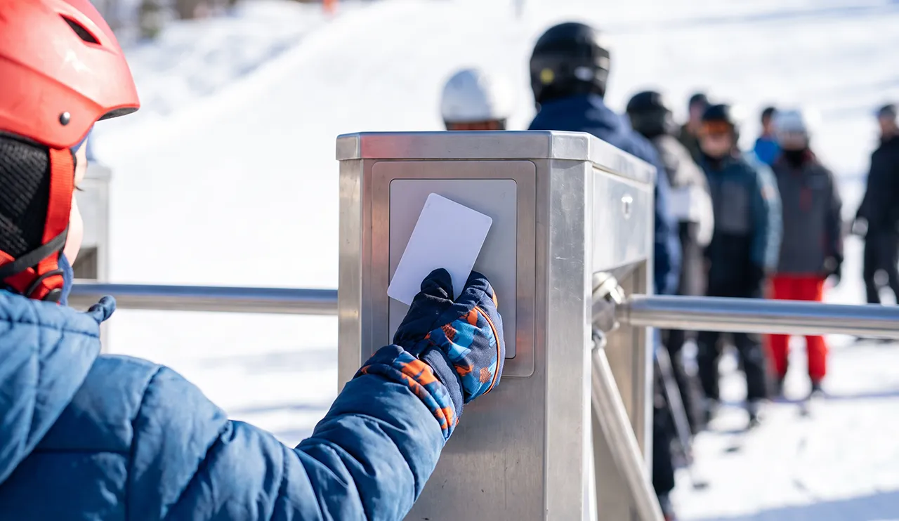 Child in a helmet scanning a lift pass at a turnstile in the French Alps