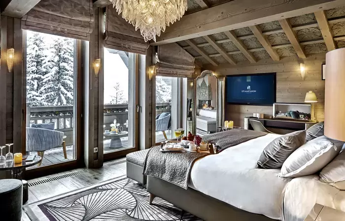 Bedroom with a crystal chandelier, beamed ceiling and balcony doors at Lys Martagon, Courchevel 1850