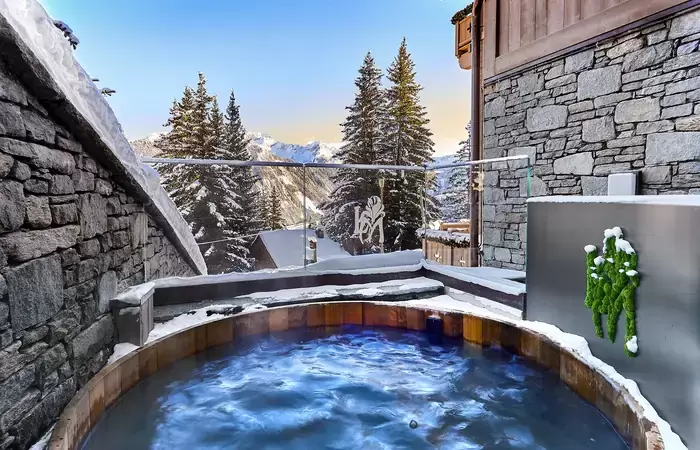 Wooden outdoor hot tub on a snowy terrace facing fir trees at Lys Martagon, Courchevel 1850