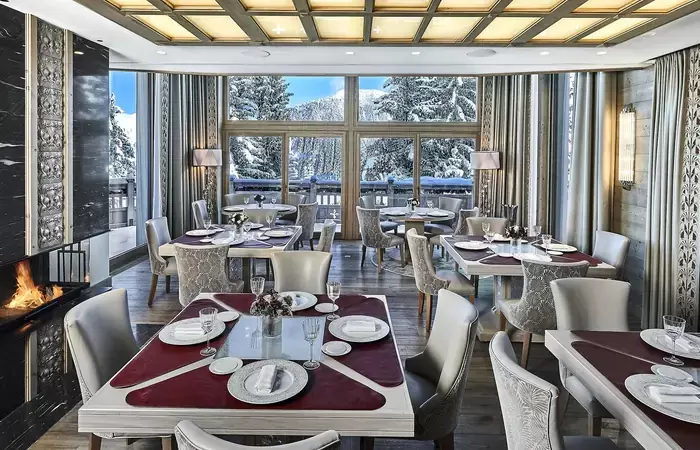Restaurant with panoramic windows onto snowy fir trees and a fireplace, Lys Martagon, Courchevel 1850