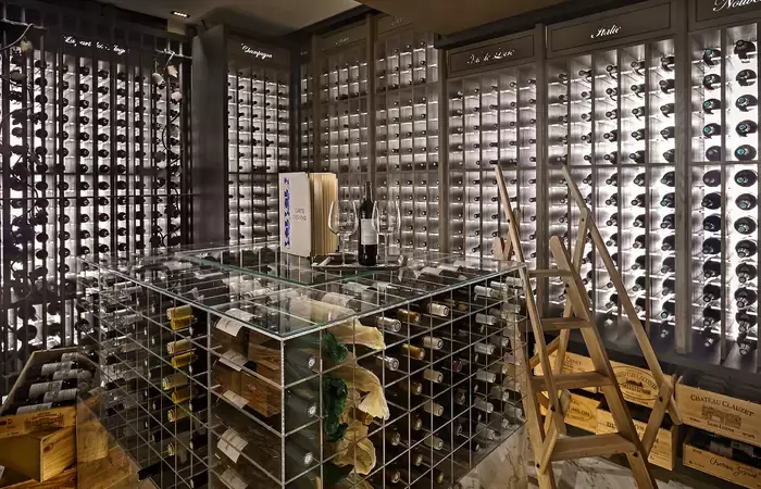 Wine cellar with illuminated bottle racks and a glass table at Lys Martagon, Courchevel 1850