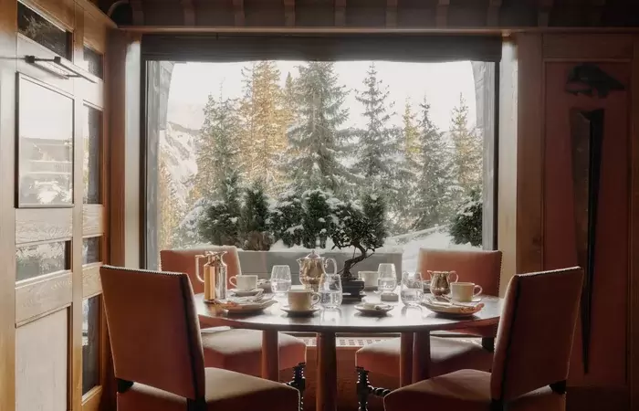 Round table set for dinner before a window onto the snowy pines