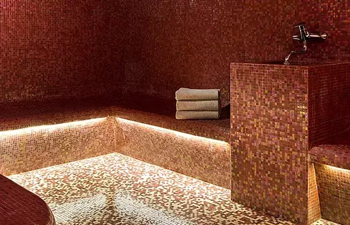 Hammam lined with red and gold mosaic and softly lit benches, Spa by Clarins at Hotel Mont-Blanc Chamonix