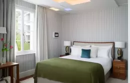 A Nest Room bed with a green throw beside the window, Chenot Palace Weggis, Lake Lucerne