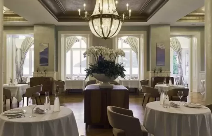 The dining room with a chandelier and white linen at Chenot Palace Weggis, Weggis