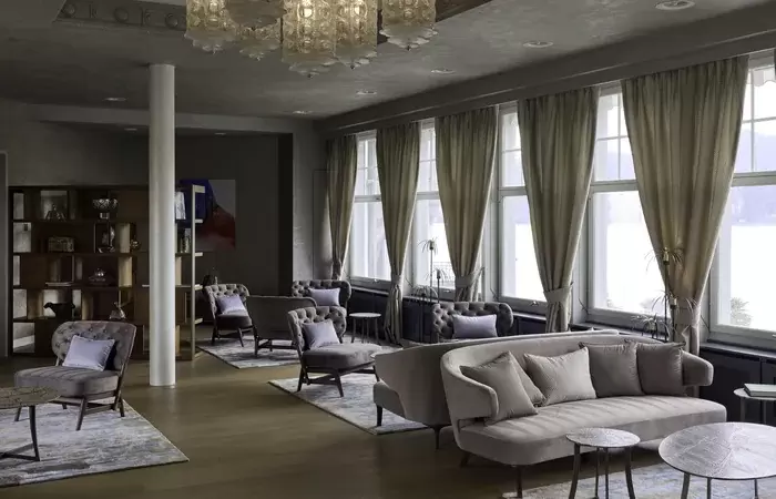 A lounge with sofas, glass chandeliers and tall windows at Chenot Palace Weggis