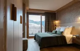 Bedroom with a dark green throw and a balcony onto the peaks in a Deluxe Apartment at Barma Residence, La Tania