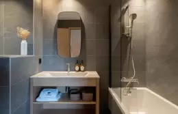 Bathroom in grey tiles with a bathtub, shower and oval mirror in a Signature Apartment, Barma Residence