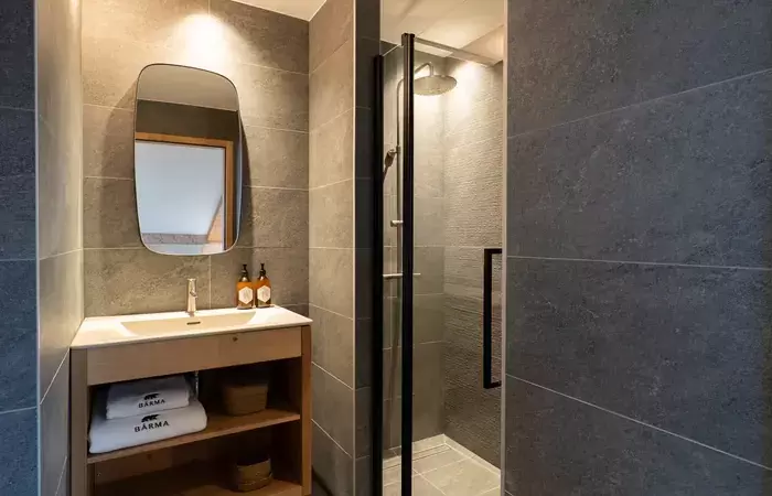 Shower room in grey stone-effect tiles with a wooden vanity at Barma Residence, Courchevel La Tania