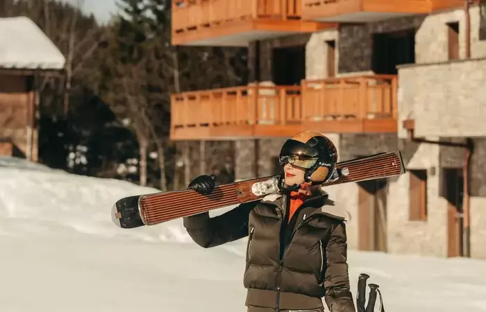 Skier carrying wooden skis past chalet balconies in Courchevel La Tania