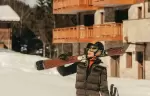 Skier carrying wooden skis past chalet balconies in Courchevel La Tania